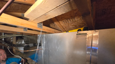 HVAC technician installing a horizontal residential air handler in a tight attic. Photo